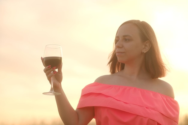 Mulher feliz com copo de vinho na zona rural Vista lateral da jovem fêmea de vestido vermelho em pé com copo de vinho tinto e desviar o olhar