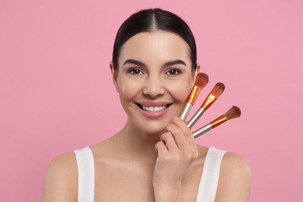 Mulher feliz com diferentes pincéis de maquiagem no fundo rosa