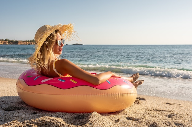 Mulher feliz com donut inflável em uma praia tropical.