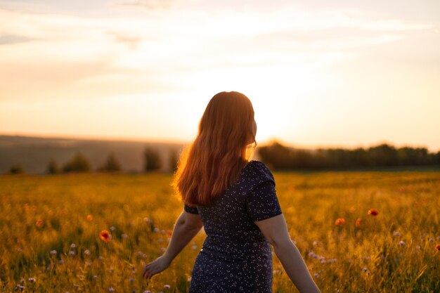 Mulher feliz com flores, apreciando o pôr do sol no campo. Turismo, viagens e conceito de estilo de vida saudável.