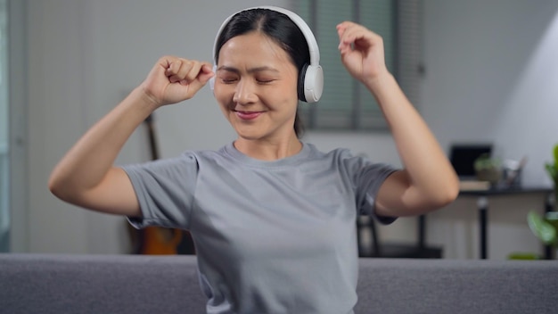 Mulher feliz com fones de ouvido e ouvindo música sentada no sofá na sala de estar em casa