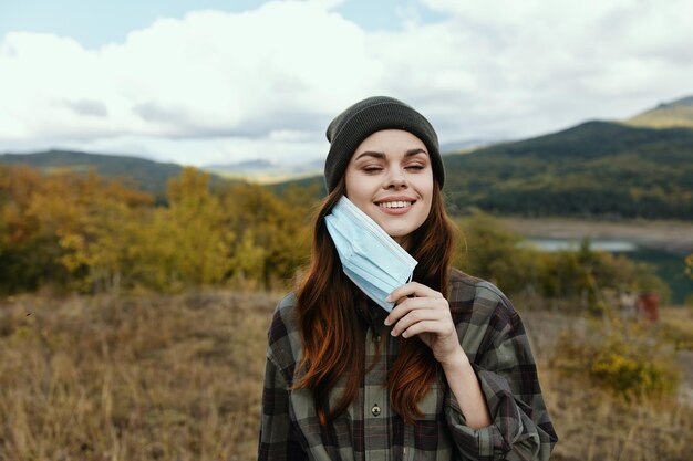 Mulher feliz com máscara médica no outono nas montanhas