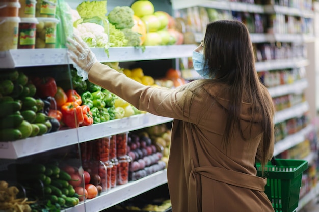 Mulher feliz com máscara protetora comendo legumes frescos enquanto esperava nas compras no supermercado