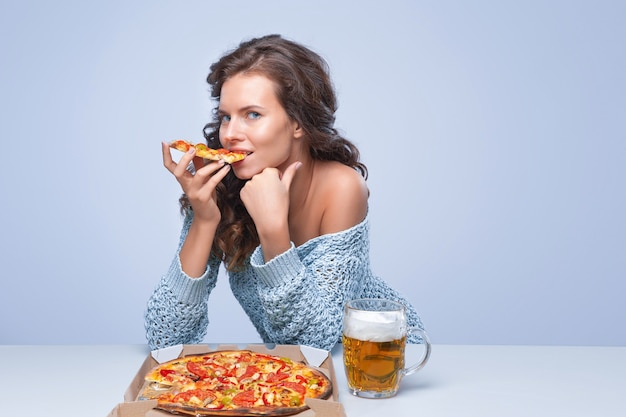 Mulher feliz com pizza e cerveja na parede cinza