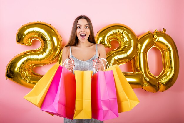 Mulher feliz com sacolas coloridas com 2020 balões de natal isolados sobre rosa