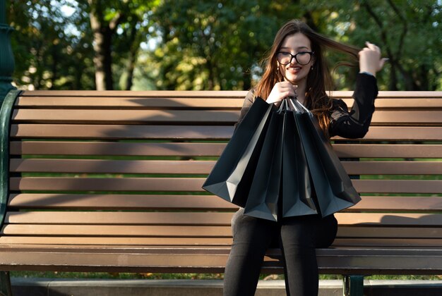 Mulher feliz com sacolas de compras no banco do parque, depois de compras bem-sucedidas.