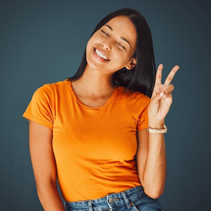 Foto mulher feliz com sinal de mão de paz e sorriso e liberdade e moda da juventude gen z isolada no fundo do estúdio mentalidade de felicidade e v emoji beleza com olhos de jovem fechados e sem preocupações