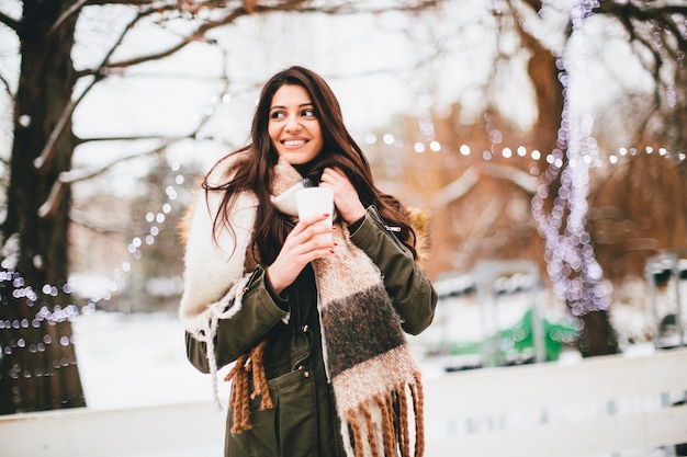 Mulher feliz com um copo de bebida quente no inverno frio ao ar livre no mercado de Natal