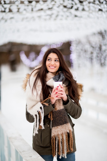 Mulher feliz com um copo de bebida quente no inverno frio ao ar livre no mercado de Natal