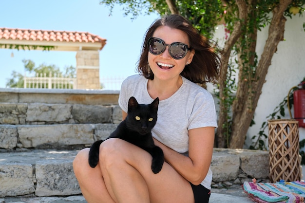 Mulher feliz com um gato preto, retrato ao ar livre do proprietário e do animal de estimação.