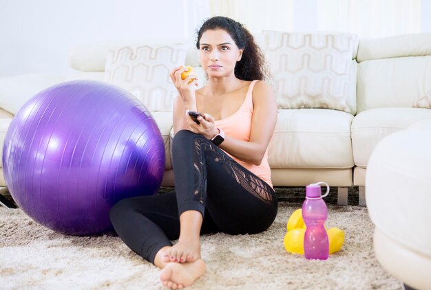 Mulher feliz come maçã enquanto descansa assistindo TV