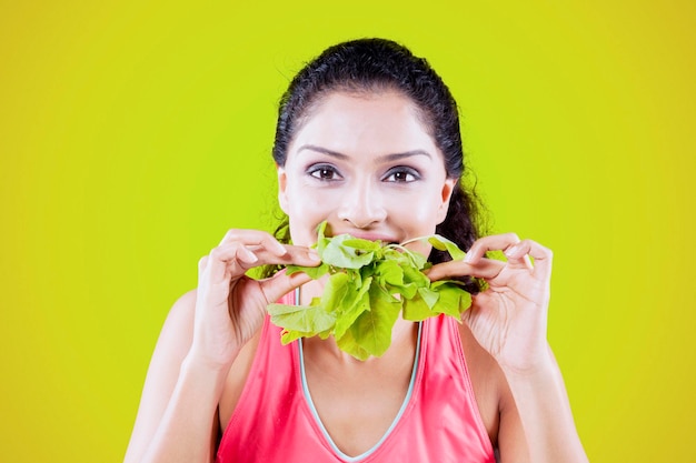 Mulher feliz comendo espinafre fresco no estúdio