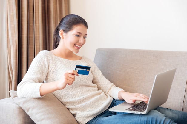 Mulher feliz comprando online no laptop com cartão de crédito em casa