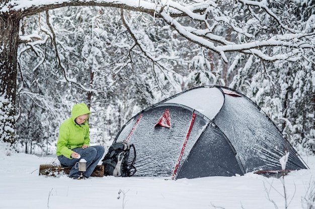 Mulher feliz cozinhando perto do acampamento de inverno na floresta de neve