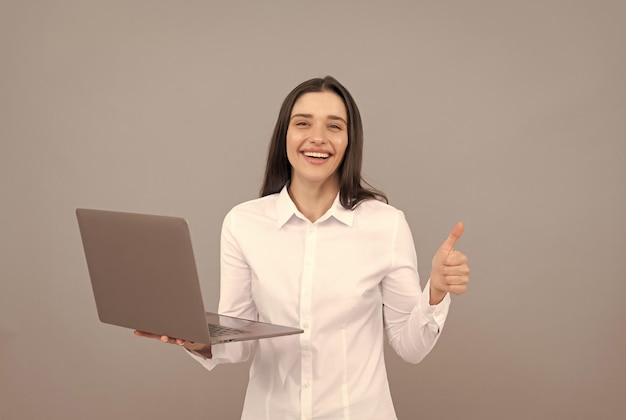 Mulher feliz de camisa branca segura computador e mostrando o polegar para cima gesto internet rápida