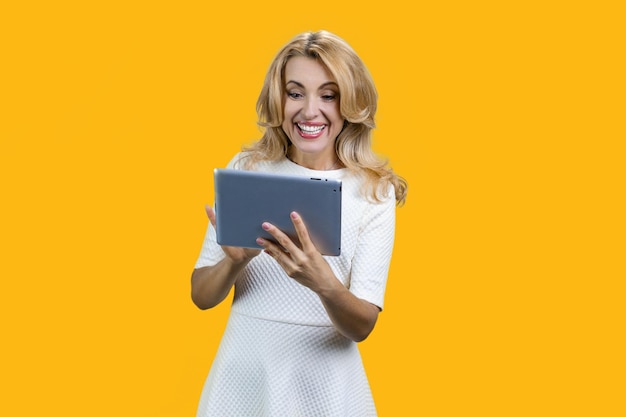 Mulher feliz de meia-idade usando tablet digital isolada em amarelo