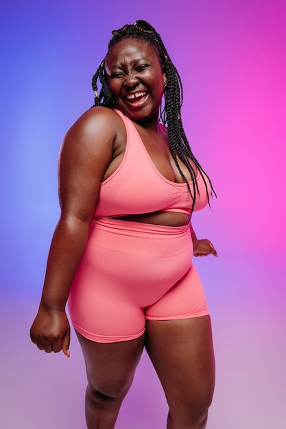 Mulher feliz de tamanho maior em roupas esportivas irradiando amor para o seu corpo enquanto dança em fundo vibrante