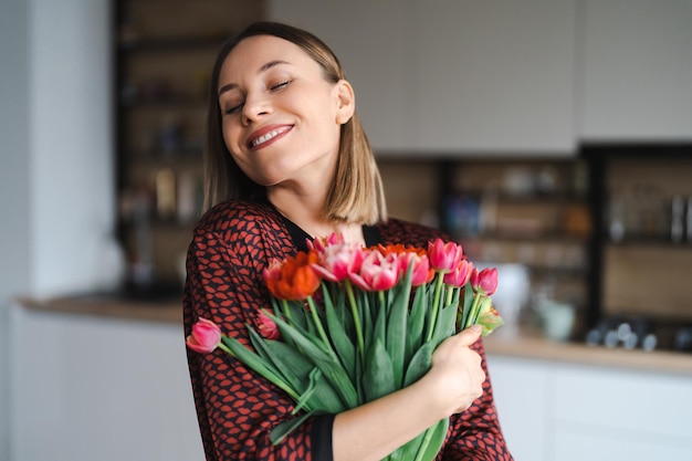 Mulher feliz desfruta de buquê de tulipas Dona de casa desfrutando de um monte de flores e interior da cozinha Doce lar Sem alergia