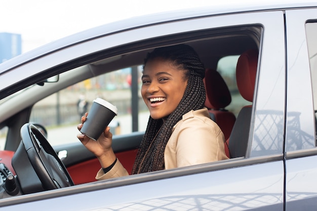 Mulher feliz dirigindo um carro tomando café, afro-americana
