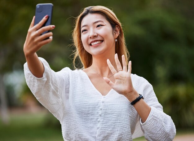 Mulher feliz e acenar olá para o telefone para blog de chamada de vídeo ou comunicação de mídia social ou postar na internet no parque Selfie rosto e menina com um sorriso para conversa de smartphone ou filme
