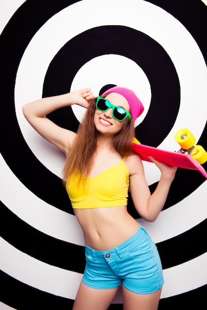 Mulher feliz e alegre de óculos segurando uma prancha de skate rosa