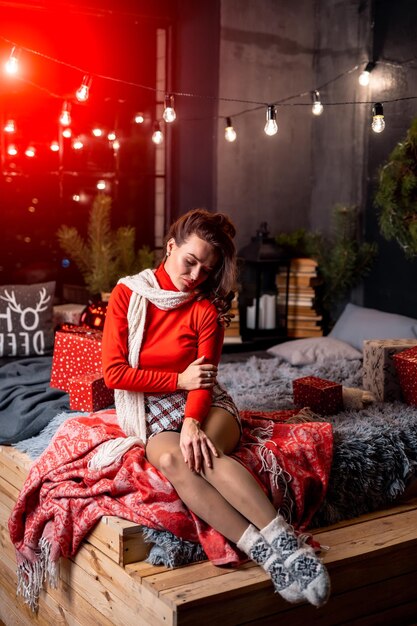 Mulher feliz e alegre sentada com presentes em uma cama Interior decorado antes das férias de inverno