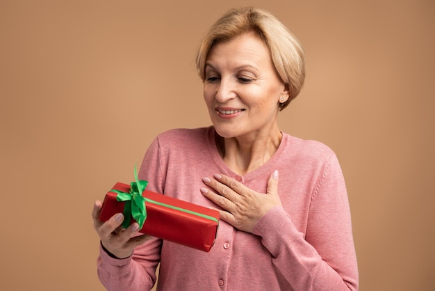 Mulher feliz e animada segurando nas mãos embrulhado a caixa de presente, olhando para ela com entusiasmo e surpresa. Estúdio interno isolado em fundo bege