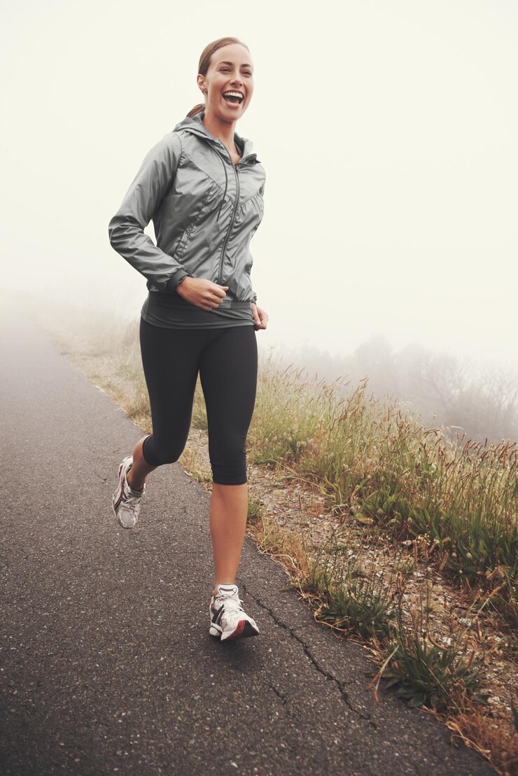 Foto mulher feliz e correndo na estrada ao ar livre no parque florestal ou na floresta para se exercitar no inverno névoa matinal e pessoa com treinamento de fitness e treino saudável no caminho no campo de montanha com sorriso