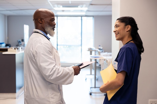 Mulher feliz e diversificada e médico sênior a falar na enfermaria do hospital, espaço de cópia. Serviços hospitalares, médicos e de saúde.