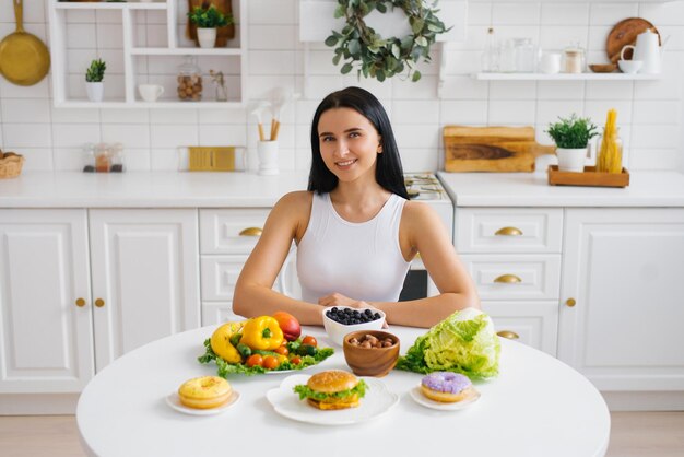 Mulher feliz e saudável está sentada em uma mesa com frutas e legumes frescos de comida saudável