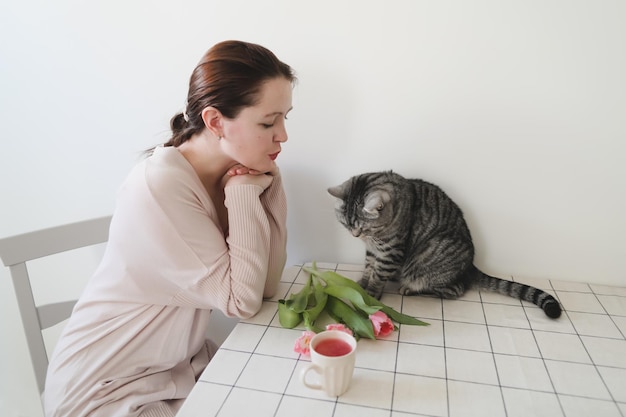 mulher feliz e seu gato cheirando tulipas cor de rosa frescas de manhã em casa