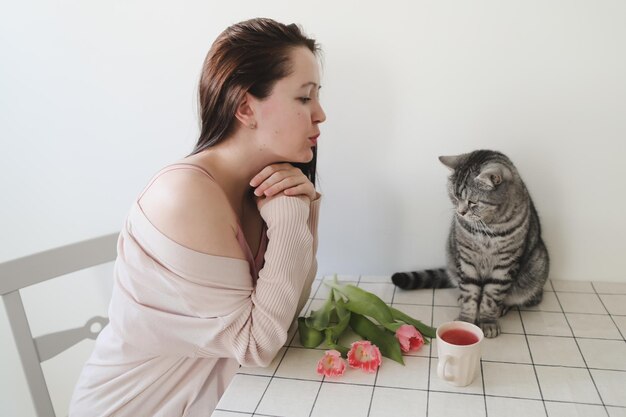 Mulher feliz e seu gato cheirando tulipas cor de rosa frescas pela manhã em casa