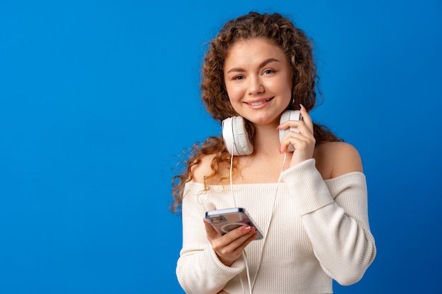 Mulher feliz e sorridente com fones de ouvido usando seu smartphone contra um fundo azul