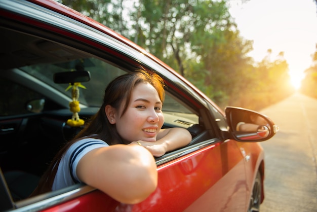 Mulher feliz e sorridente em um carro vermelho com a luz do sol