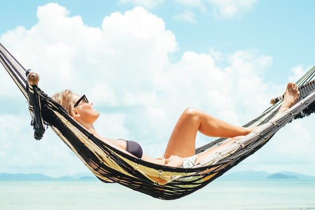 Mulher feliz em biquíni preto relaxando na rede