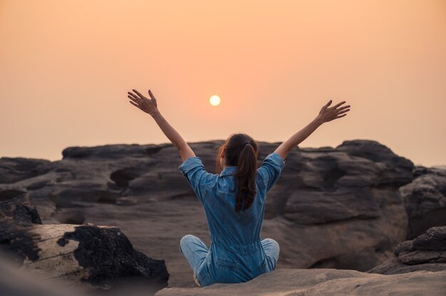 Mulher feliz em camisa jeans levantando os braços e vendo o pôr do sol no desfiladeiro do parque nacional