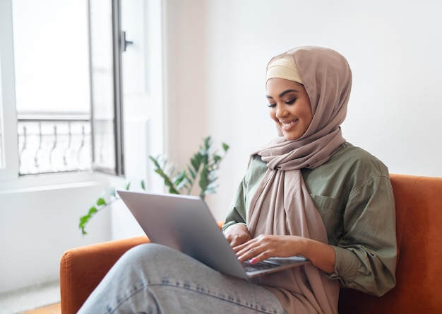 Mulher feliz em hijab trabalhando on-line no laptop em casa