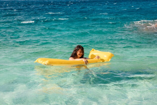 Mulher feliz em maiô azul flutuando no colchão inflável amarelo