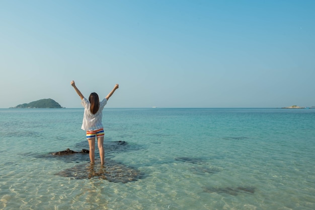 Mulher feliz em pé com os braços estendidos na praia no mar