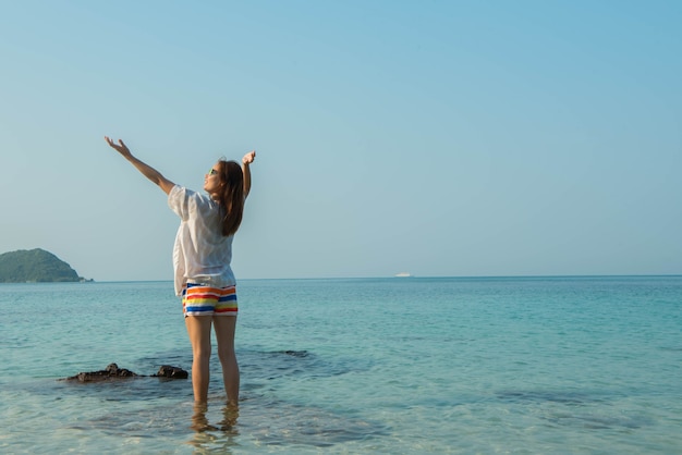 Mulher feliz em pé com os braços estendidos na praia no mar