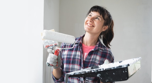 Mulher feliz em rolo de pintura e tinta branca para paredes em retrato de closeup de mãos Trabalhos de construção e reparos cosméticos em pintura de parede de casa, acabamento de acabamento com suas próprias mãos