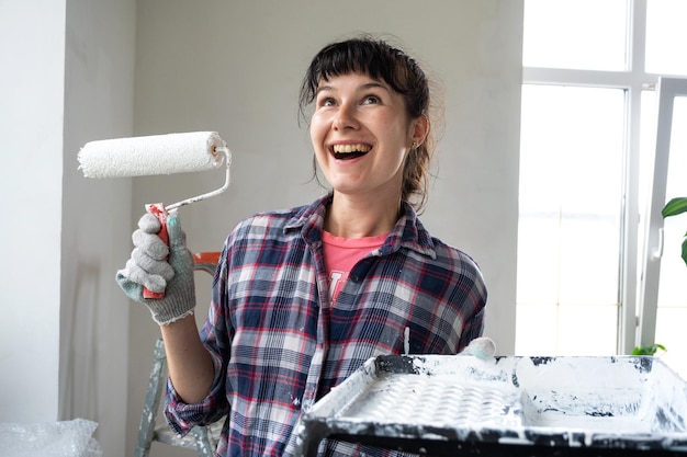 Mulher feliz em rolo de pintura e tinta branca para paredes em retrato de closeup de mãos Trabalhos de construção e reparos cosméticos em pintura de parede de casa, acabamento de acabamento com suas próprias mãos