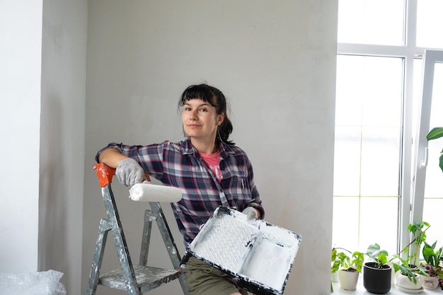 Mulher feliz em rolo de pintura e tinta branca para paredes em retrato de closeup de mãos Trabalhos de construção e reparos cosméticos em pintura de parede de casa, acabamento de acabamento com suas próprias mãos