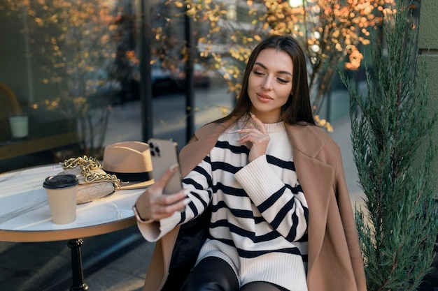 Mulher feliz em roupas casuais sorrindo conversando andando bebendo café conversando online tirando selfie usando apenas o celular