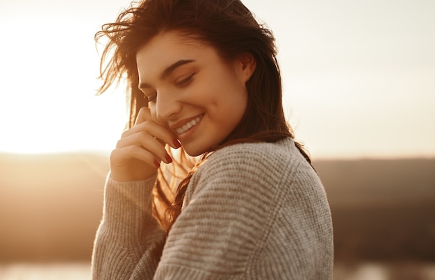 Mulher feliz em suéter curtindo o pôr do sol na natureza