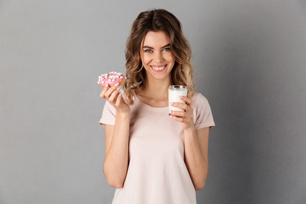 Mulher feliz em t-shirt mostrando donut e copo de leite enquanto mais cinza