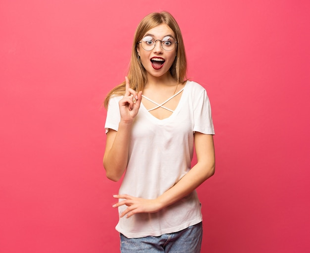 Mulher feliz em t-shirt, posando com o braço na cintura, tendo uma ideia e olhando para a câmera sobre o fundo rosa.