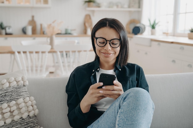 Mulher feliz está conversando no telefone em casa Garota está enviando mensagens de texto e sorrindo recebendo mensagens