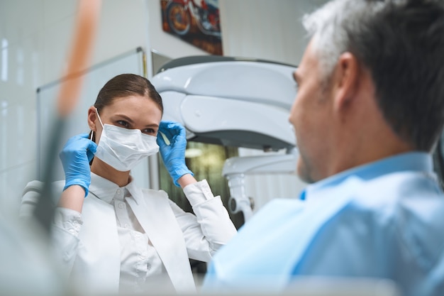 Mulher feliz está usando máscara e luvas esterilizadas enquanto trata de problemas dentais masculinos no consultório