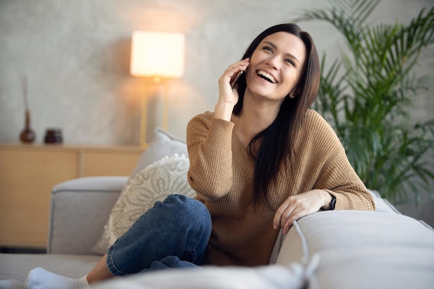 Mulher feliz falando ao telefone em casa, senhora alegre desfruta de uma agradável conversa móvel fazendo ligação por telefone